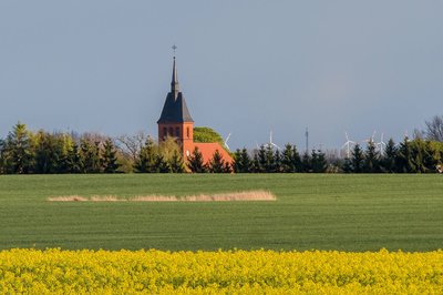 ein Feld mit roter Kirche und Bäumen im Hintergrund