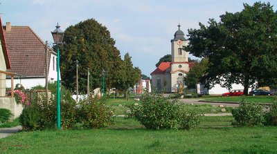 ein Feld mit Bäumen und einer Kirche, sowie Häusern im Hintergrund