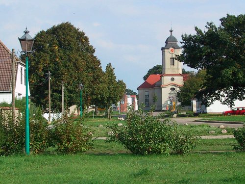ein Feld mit Bäumen und einer Kirche, sowie Häusern im Hintergrund